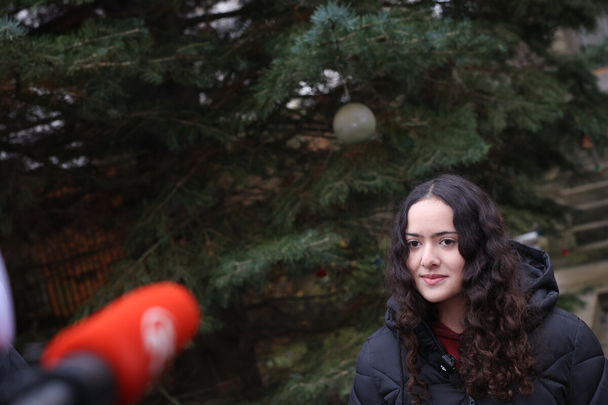 Внучка Ольга на фоні ялинки, що невдовзі стане головною різдвяною прикрасою Львова, розповідає журналістам історію родинного дерева
